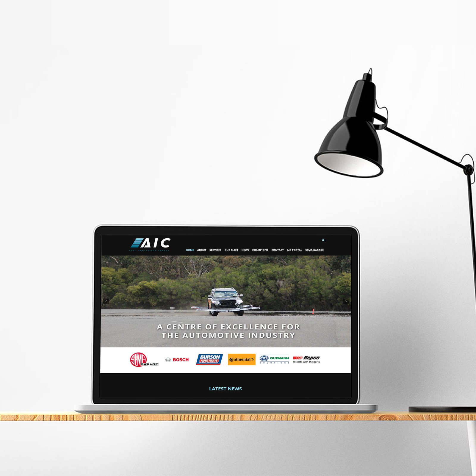 A laptop on a desk displays a car on the screen, accompanied by a lamp, symbolizing automotive innovation and e-commerce.