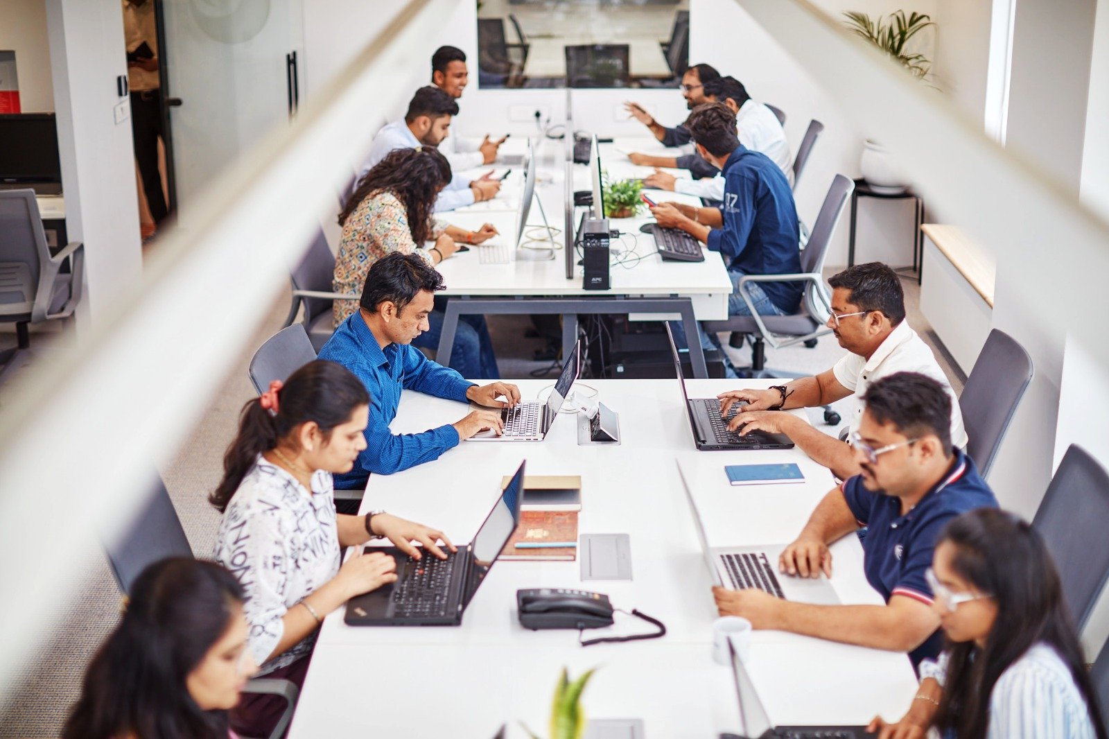 A lively office scene with individuals using laptops, showcasing teamwork and creativity in a dynamic work environment.